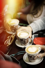 group of people drinking coffee holding coffee cups with cappuccino marked with hearts