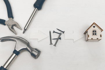 Home house construction concept background with copy space. Hammer and nails and toy house on white wooden table board backgroud.