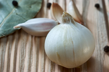 On the wooden table, seasonings: onion, garlic, black pepper peas and bay leaf