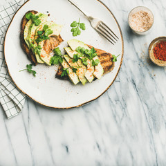 Healthy vegan breakfast or lunch. Flat-lay of avocado toast on plate with seasoning and glass of lemon water over marble background, top view, copy space, square crop. Clean eating, detox food concept