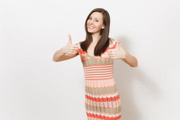 Beautiful young brunette girl in light beige and pink patterned dress rejoices, smiling and shows gestures thumbs up in studio on white background. Concept of good mood. Copy space for advertisement.