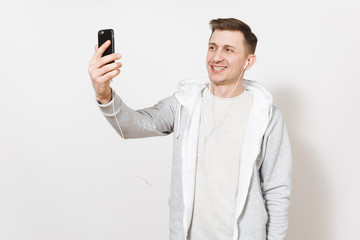 Young handsome smiling man student in t-shirt, blue jeans and light sweatshirt takes himself on phone during call with headphones in studio on white background. Concept of communication, good mood