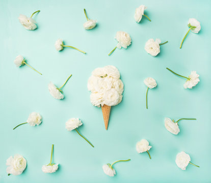 Fototapeta Flat-lay of waffle sweet cone with white buttercup flowers over light blue background, top view. Spring or summer mood concept