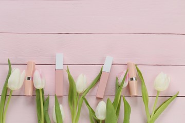 Beige lip gloss and lipstick color nude  in gently pink tulip flowers  on a pink wooden plank background. Cosmetics in pastel colors