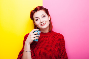 Happy woman with a cup of tea in hands looking at the camera on two colored background in yellow and pink