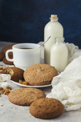 Cup of black coffee in a white cup, Bottles with milk, oatmeal cookies, oatmeal, raisins on a light background. Scene from breakfast