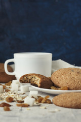 Cup of coffee with milk in a white cup, Bottles with milk, oatmeal cookies, oatmeal, raisins on a light background. Scene from breakfast