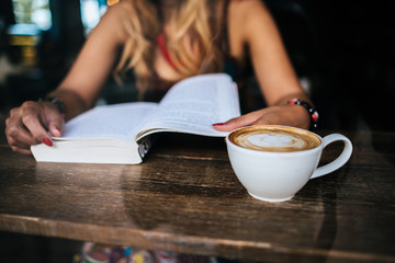 Young woman  reading book and fresh cup of coffee on the table