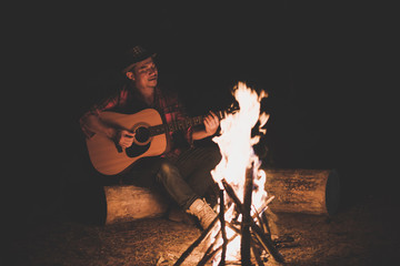 Young men. sitting around camp fire playing guitar