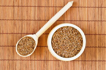 Flax seeds in bowl and in wooden spoon on bamboo napkin