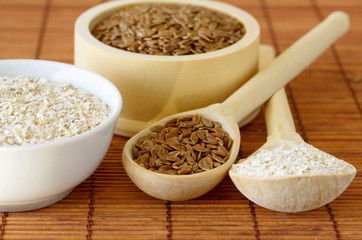 Flax seeds and oat bran in bowls and wooden spoons on bamboo napkin