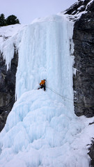 male ice climber gets ready to climb a steep frozen candle on an ice fall in the Alps near Davos