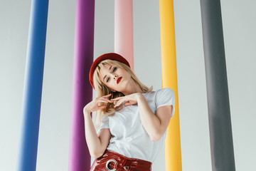 Attractive young woman in red and white clothes by colorful columns isolated on grey