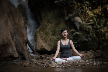 Young woman in yoga pose sitting near waterfall