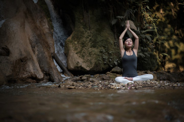 Young woman in yoga pose sitting near waterfall