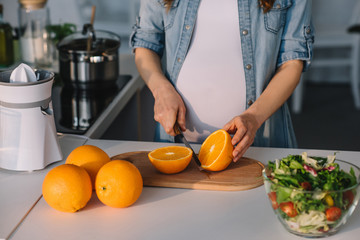 cropped image of pregnant woman cutting oranges at kitchen