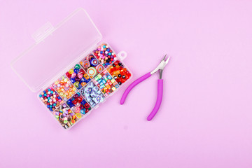 Сolored beads and pliers on pink background