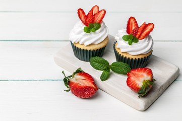 Vanilla cupcakes with strawberry on a light wooden background