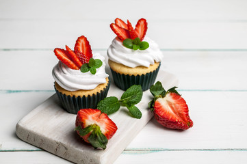 Vanilla cupcakes with strawberry on a light wooden background