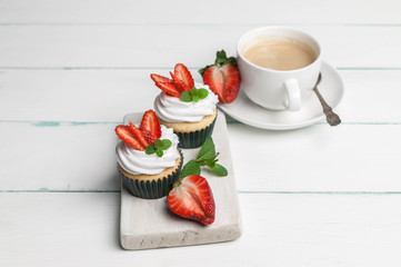 Vanilla cupcakes with strawberry and cup of coffee on a light wooden background