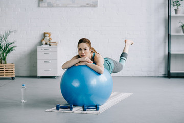 beautiful pregnant woman exercising on fitness ball in living room