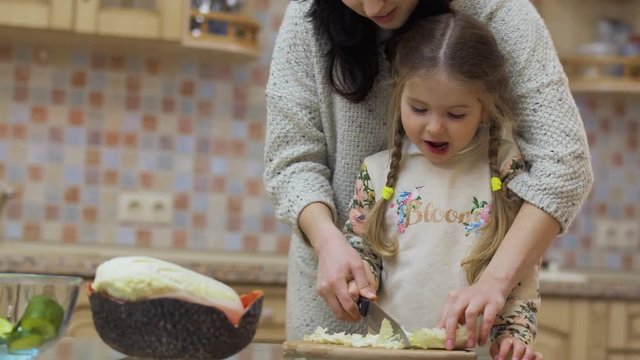 Young woman teaches her daughter to cut cabbage for salad