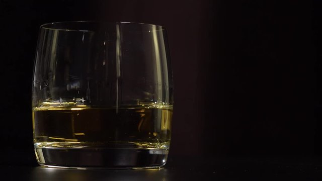 A man puts a glass of whiskey on a table - closeup - dark background