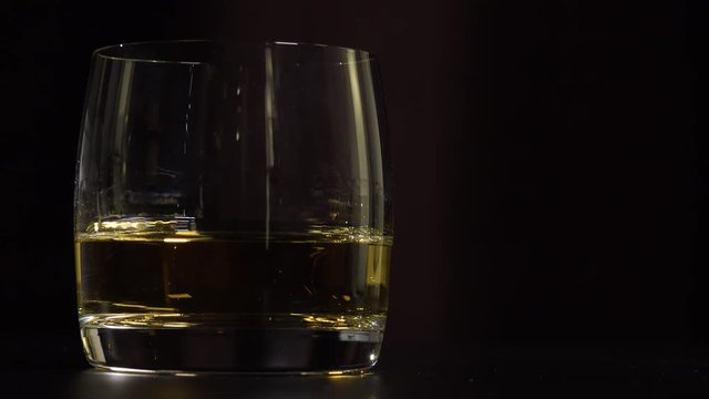 A man lifts a glass of whiskey from a table - closeup - dark background