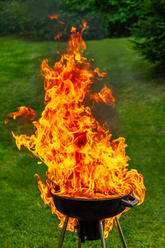 A big fire flashover a black grill outdoors when having a barbeque.