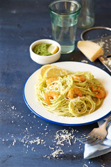 Spaghetti with green pesto, shrimps and cheese. Blue wooden background
