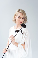 beautiful blonde girl posing in white blouse with black rose, isolated on grey