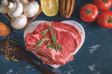 Cuts of beef for grilling on a wooden cutting Board with the Bay leaf, rosemary, olive oil and Provencal herbs for the marinade in a rustic style. Copy spase
