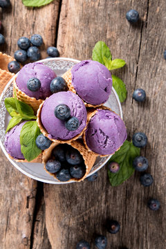 Ice cream. Blueberry scoop in cone on wooden table.