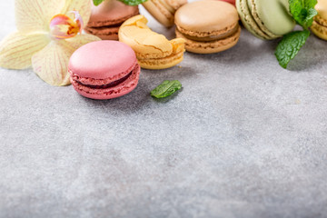 French assorted macarons with mint leaves on light gray concrete background. Holidays food concept with copy space.