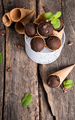 Chocolate ice cream scoop in cone on wooden table. Sweet desert.