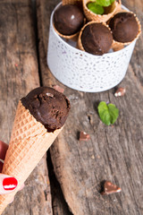Chocolate ice cream scoop in cone on wooden table. Sweet desert.