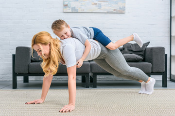 Smiling mother doing plank with little boy on back