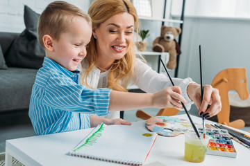 Happy mother and little son dipping paintbrushes into water