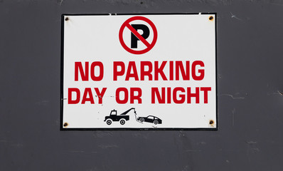 No parking day or night with tow truck icon symbol sign on a metal gate entrance