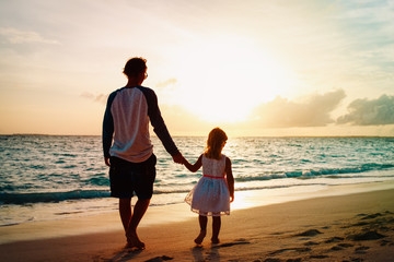 father and daughter walking on beach at sunset
