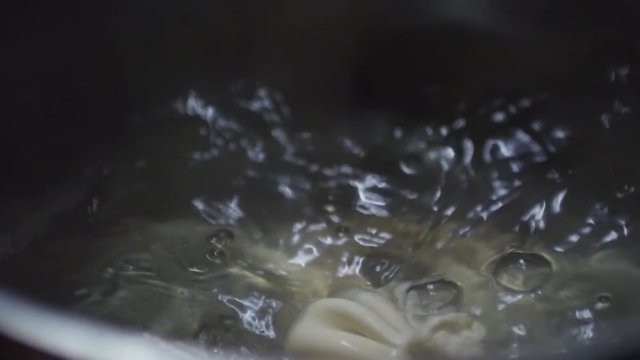 Close up with slow motion of unrecognizable cook putting khinkali dumplings into boiling water