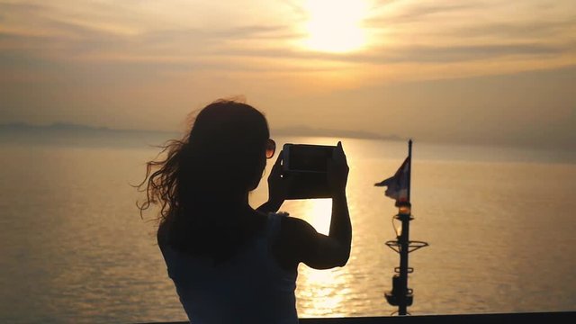 Silhouette of girl takes photos of sunset on mobile phone camera while traveling on cruise ship. slow motion. 1920x1080