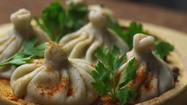 Close up of spinning wooden plate of delicious khinkali dumplings seasoned with chili pepper and decorating with fresh parsley