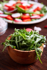 Obraz na płótnie Canvas Fresh ruccola in a wooden bowl on wooden table over vegetable background, shallow depth of field.