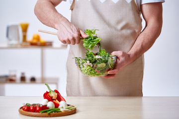 Man cooking at kitchen making healthy vegetable salad, close-up, selective focus.