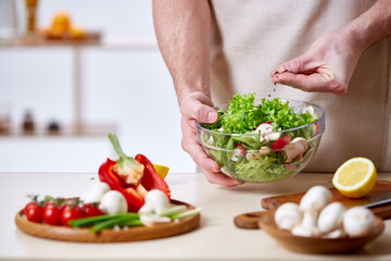 Man cooking at kitchen making healthy vegetable salad, close-up, selective focus.