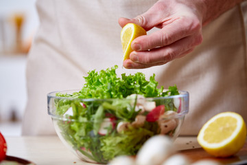 Man cooking at kitchen making healthy vegetable salad, close-up, selective focus.