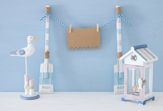 nautical concept with hanging empty note on a string next to beach house and seagull over blue background.