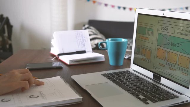 Freelancer's workplace. Web Developer makes sketches of the site in his notebook working remotely from home office