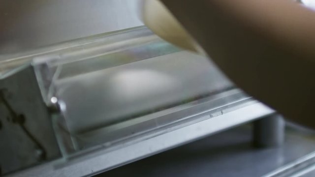Unrecognizable female cook putting dumpling wrapper into dough sheeter machine to flatten it